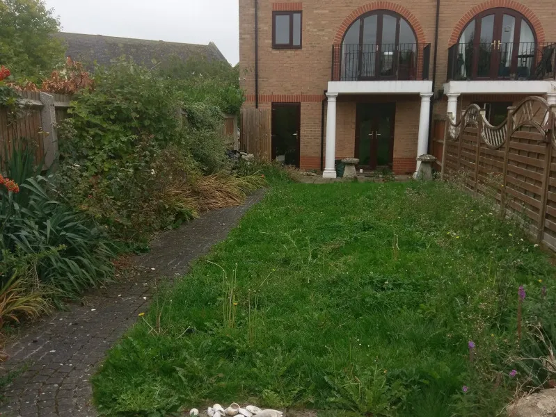 Overgrown grass and flowerbeds, this time looking towards the house and its balcony