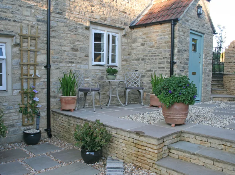 A small bistro set on a patio of Cotswold stone slabs surrounded by gravel and small planters